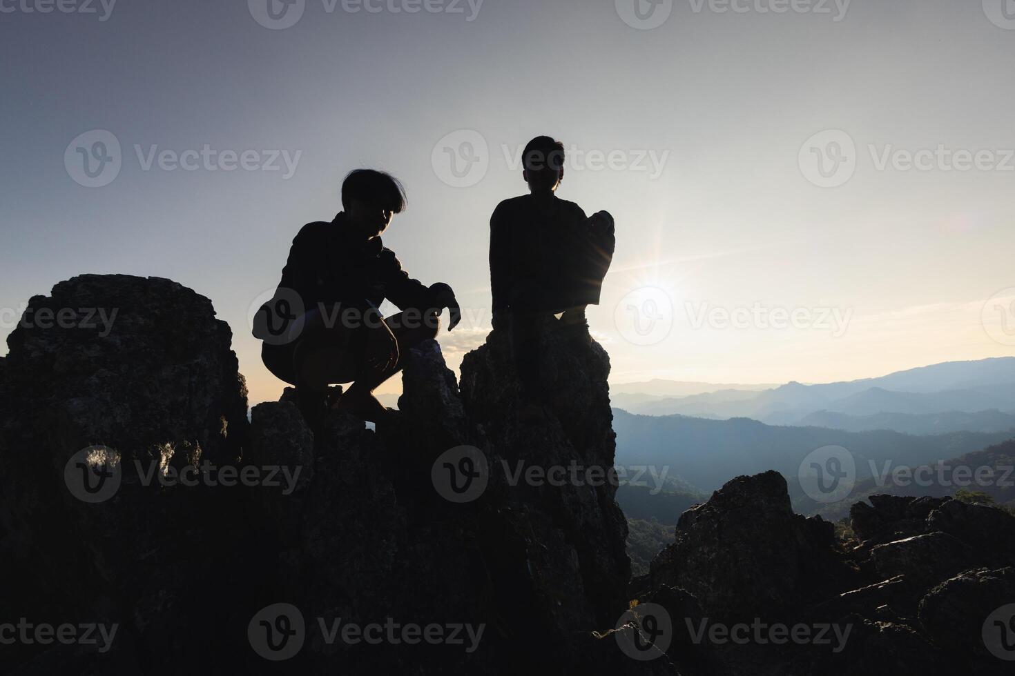 person på topp av fjäll, silhuett av ung människor Sammanträde på en sten ser till de horisont. foto