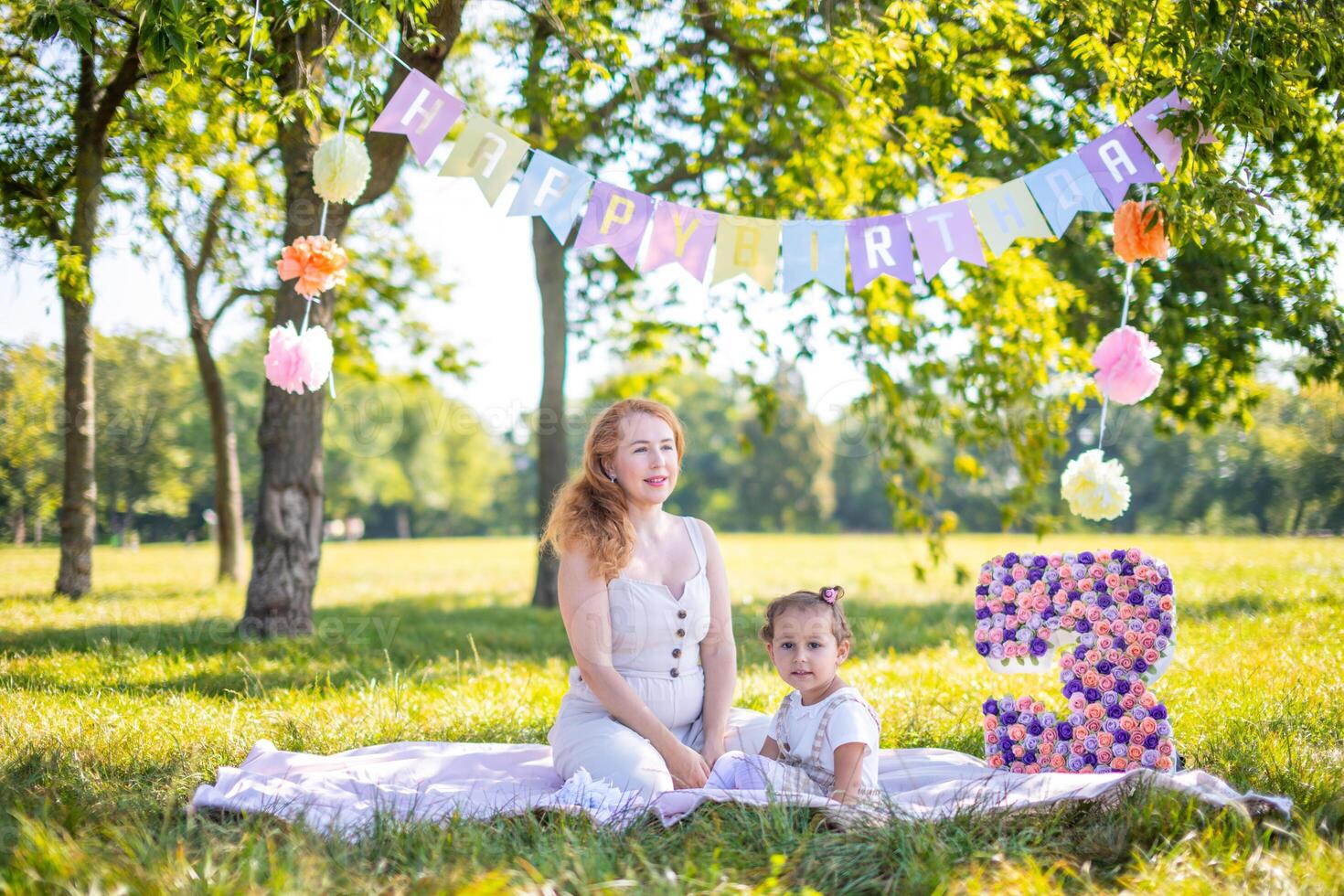 glad mor och dotter har roligt på barn födelsedag på filt med papper dekorationer i de parkera foto