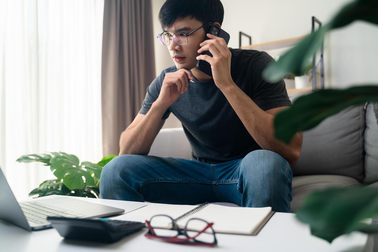 de man i tillfällig kläder arbetssätt med en bärbar dator, dator, smart telefon, kalkylator Sammanträde på de soffa i de levande rum på Hem, arbetssätt från Hem begrepp. foto