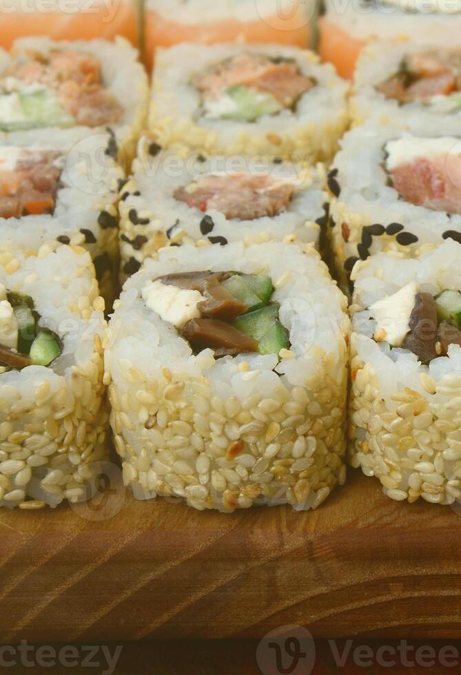 närbild av en massa av sushi rullar med annorlunda fyllningar lögn på en trä- yta. makro skott av kokta klassisk japansk mat med en kopia Plats foto