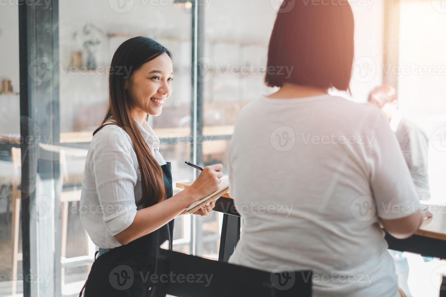 leende kvinna servitris ta beställa prata till klienter Kafé restaurang besökare kvinna, vänlig professionell kvinna server ha på sig förkläde skriva middag mat meny val, tjänande personal Bra kund service foto