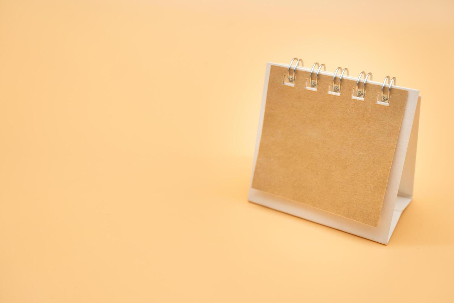 tom kalender med brun papper isolerat på orange bakgrund. tom papper skrivbord spiral kalender. stänga upp av en tom återvinna papper mall. foto