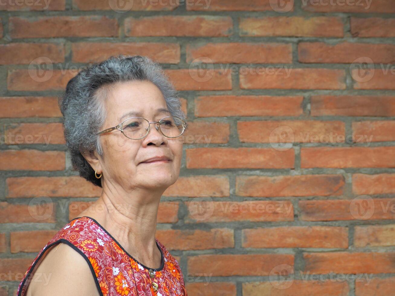 senior kvinna leende och ser bort medan stående med en tegel vägg bakgrund. Plats för text. foto