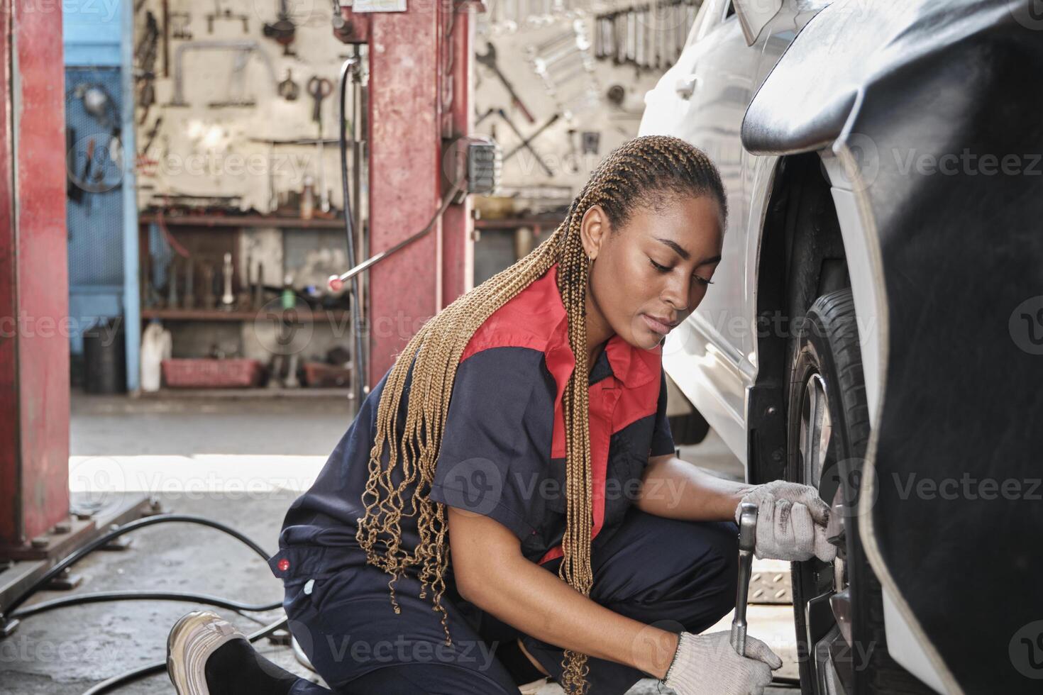 ett afrikansk amerikan kvinna bil- mekaniker arbetstagare skruvar bil hjul nötter med rycka för reparera på garage, professionell arbetskraft Arbetar, fordon underhåll service jobb, industri ockupation företag. foto