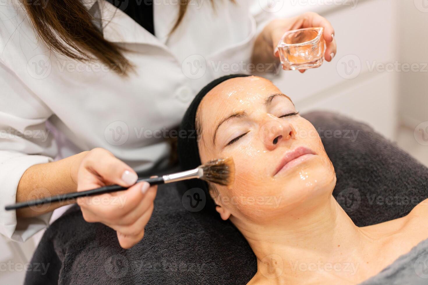 beskära kosmetolog applicering grädde på ansikte av klient foto