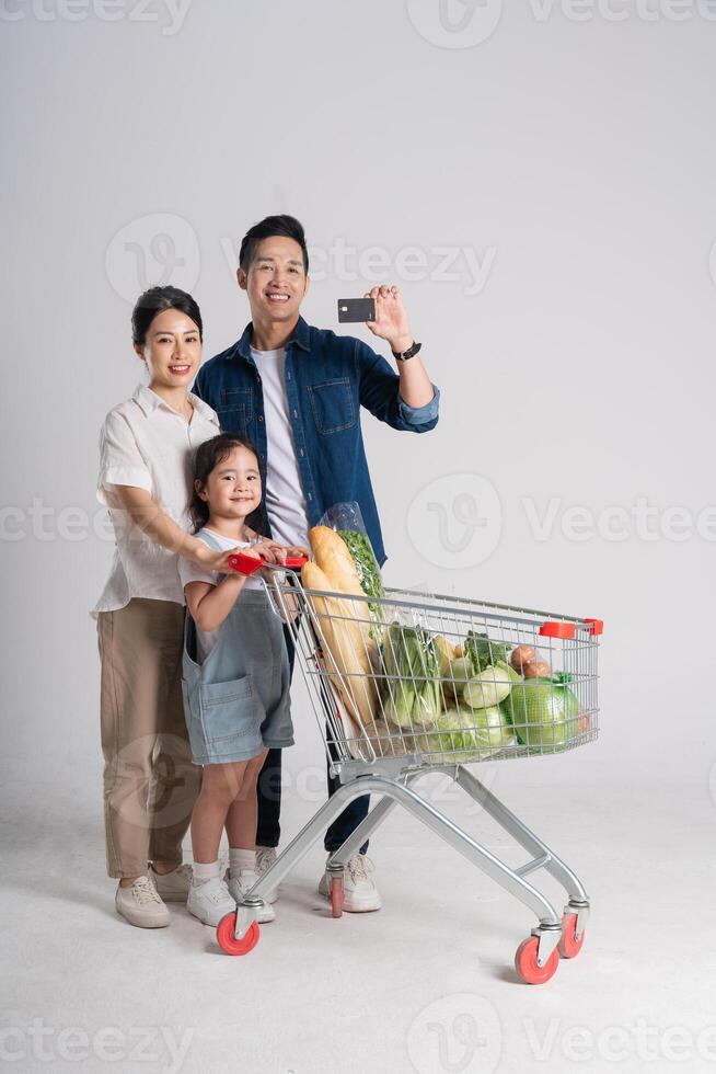 bild av asiatisk familj tryckande en mataffär vagn medan handla, isolerat på vit bakgrund foto