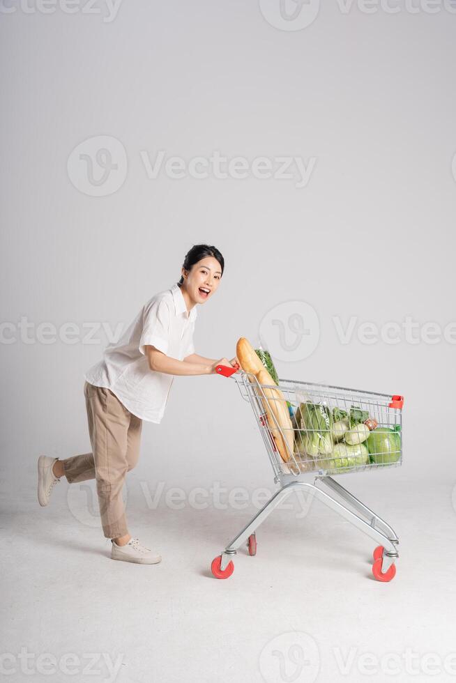 leende kvinna lyckligt tryckande en mataffär vagn, isolerat på vit bakgrund foto