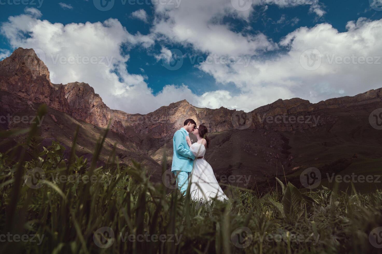 en ung man och hans fru stå i ett omfamning hög i de bergen mot de bakgrund av episk stenar på en solig dag. nygifta bröllop par i de bergen foto