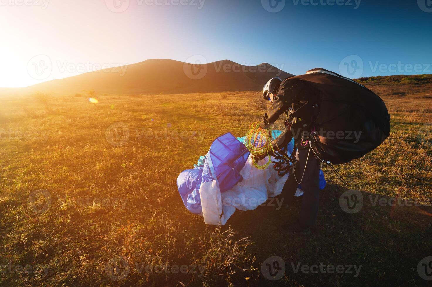 en ung manlig paraglider på solnedgång i de bergen samlar hans paraglider till ta den till de startande punkt. skärmflygning sport foto