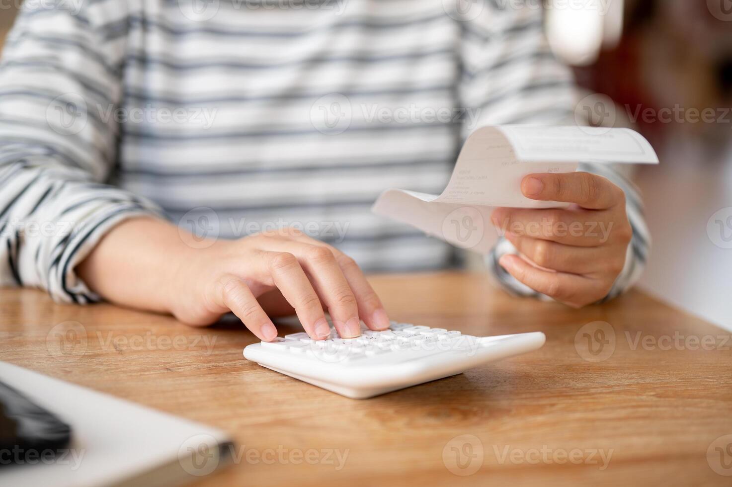 en kvinna använder sig av en kalkylator på en tabell, beräknande henne hushåll kostnader och räkningar. foto