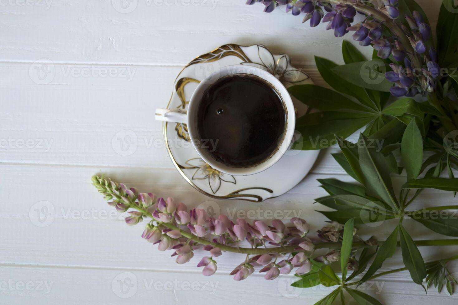 en kopp av kaffe och lupin blommor på en vit trä- tabell. foto