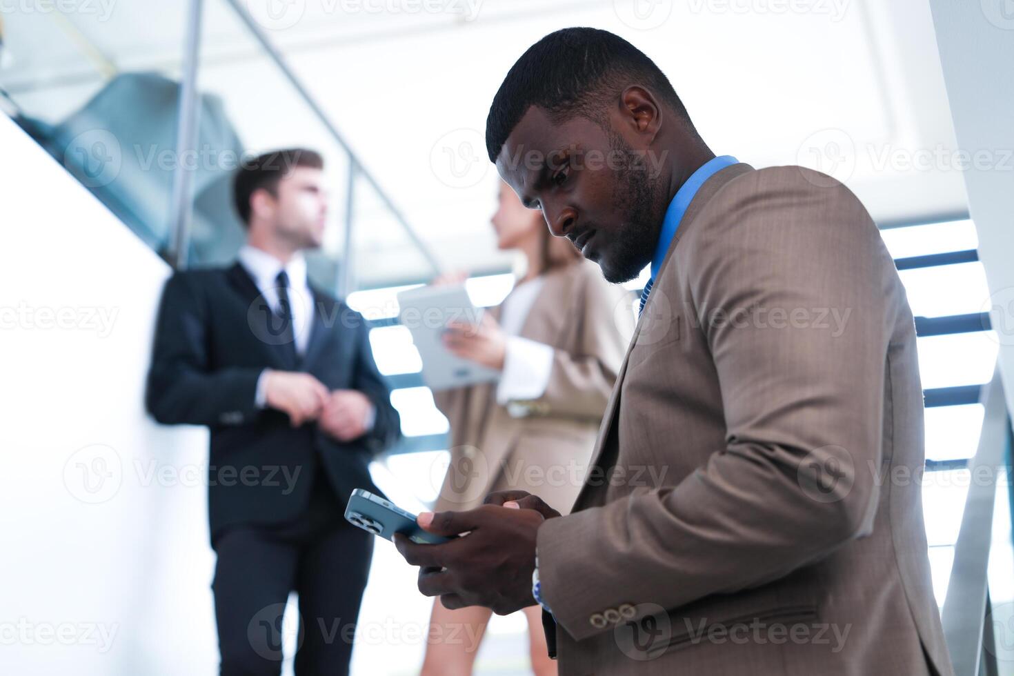 smart svart affärsman tittar på mobil telefon. skallig vuxen man bär formell ha på sig. omtänksam afrikan-amerikan affärsman i en perfekt skräddarsydd kostym stående i trappa i kontor. foto