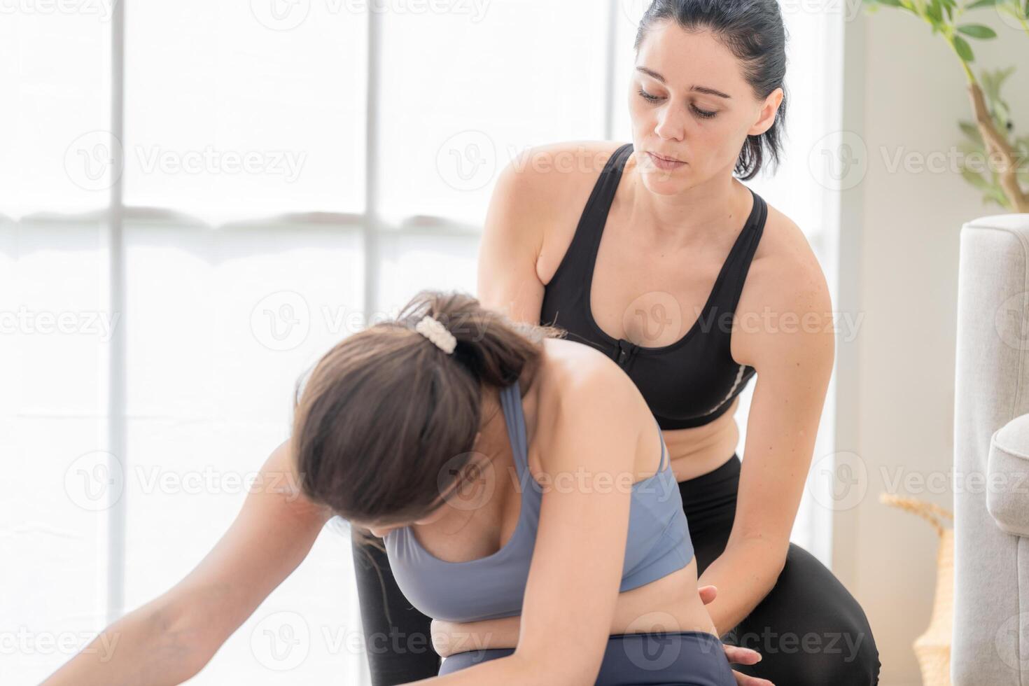 två kvinnor självsäker Träning yoga. atletisk kvinnor i sportkläder håller på med kondition stretching övningar på Hem i de levande rum. sport och rekreation begrepp. yoga lärare är portion ung kvinna. foto