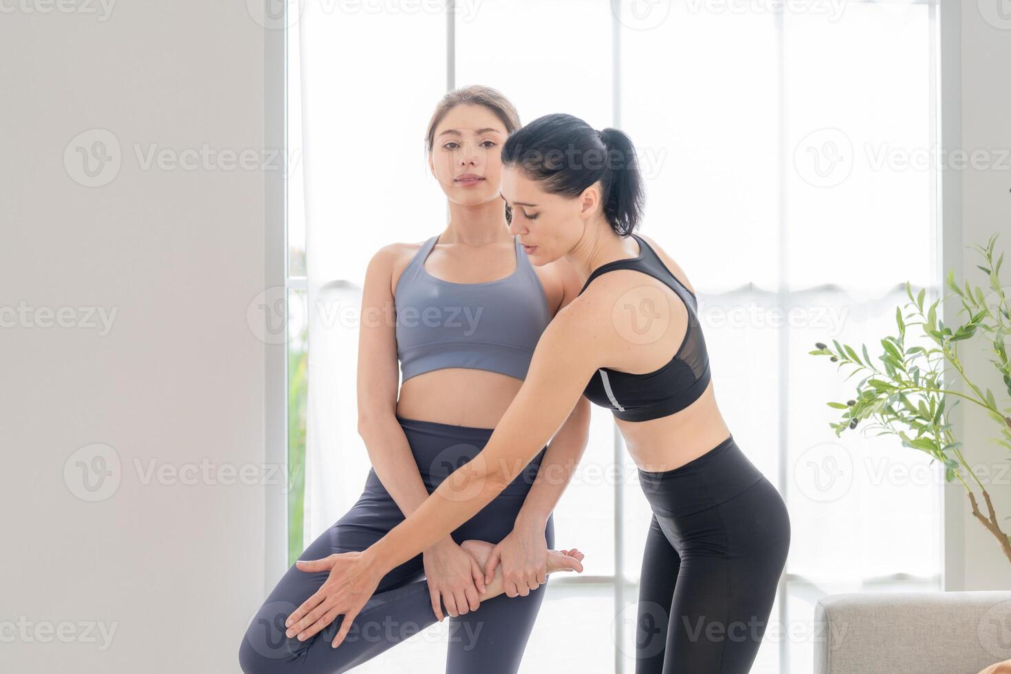 två kvinnor självsäker Träning yoga. atletisk kvinnor i sportkläder håller på med kondition stretching övningar på Hem i de levande rum. sport och rekreation begrepp. yoga lärare är portion ung kvinna. foto