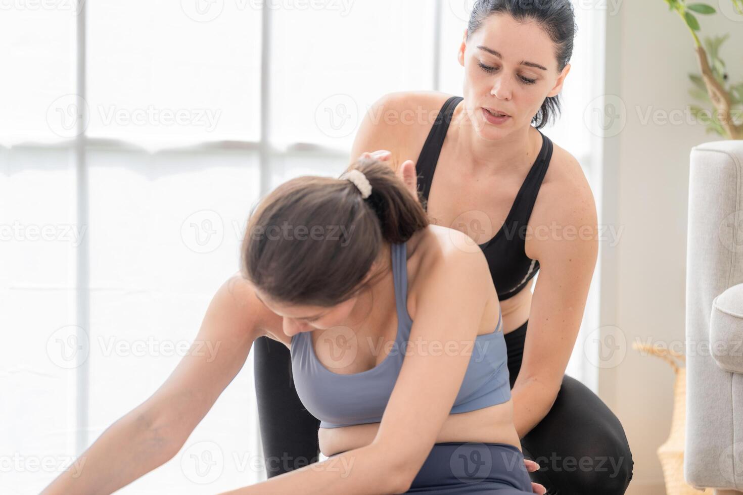 två kvinnor självsäker Träning yoga. atletisk kvinnor i sportkläder håller på med kondition stretching övningar på Hem i de levande rum. sport och rekreation begrepp. yoga lärare är portion ung kvinna. foto