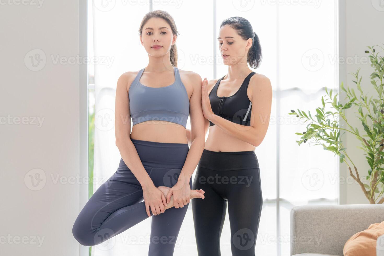 två kvinnor självsäker Träning yoga. atletisk kvinnor i sportkläder håller på med kondition stretching övningar på Hem i de levande rum. sport och rekreation begrepp. yoga lärare är portion ung kvinna. foto
