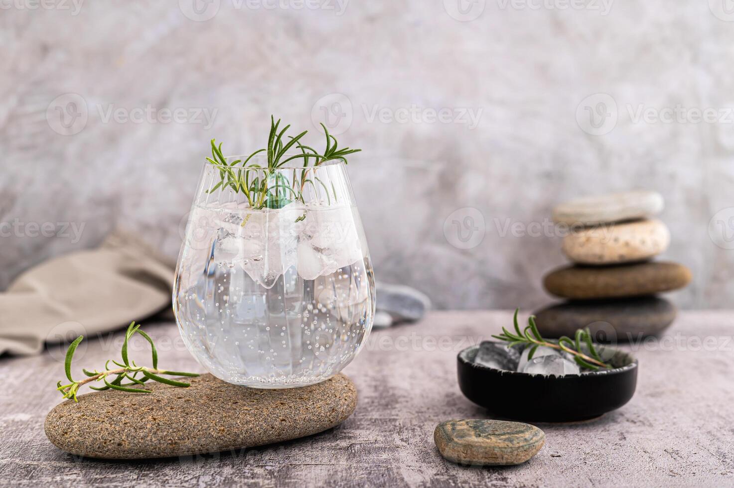 gin tonic med is och rosmarin i en glas på en sten på de tabell foto