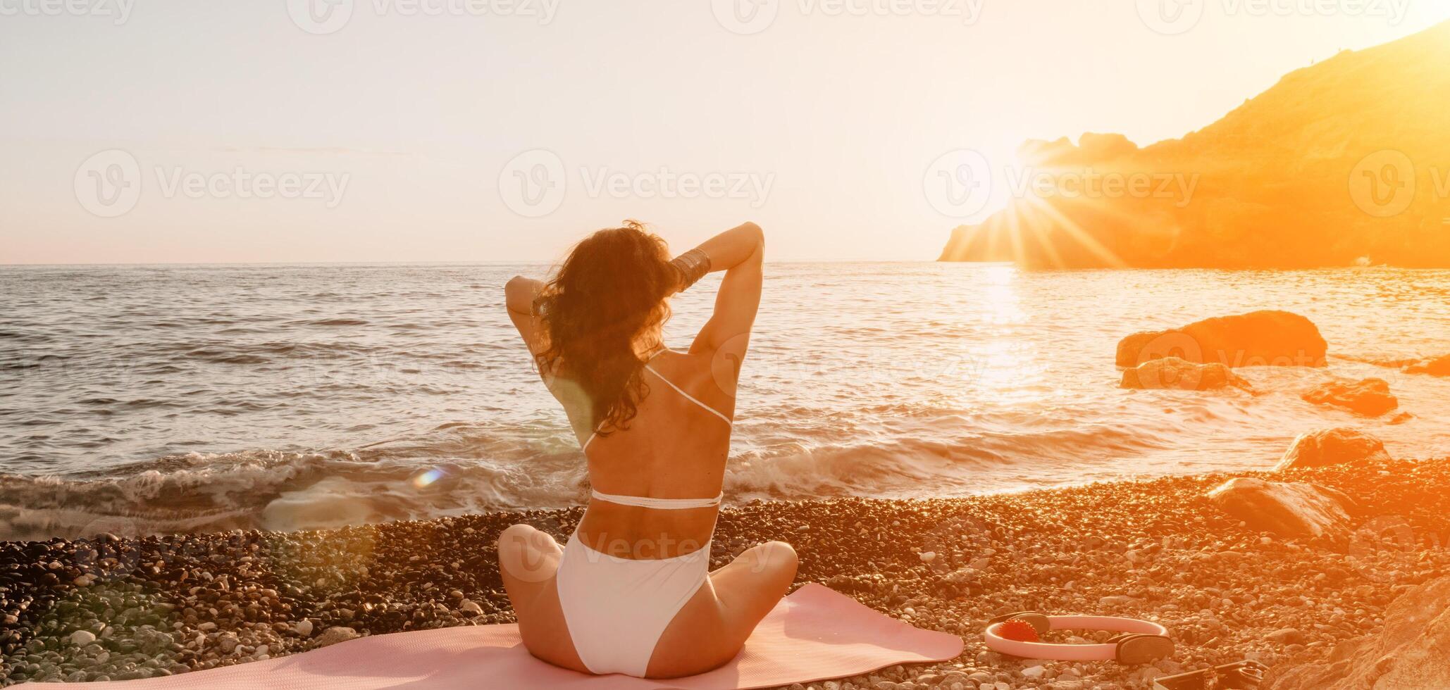kvinna hav yoga. Lycklig kvinna i vit baddräkt och boho stil armband praktiserande utomhus på yoga matta förbi hav på solnedgång. kvinnor yoga kondition rutin. friska livsstil, harmoni och meditation foto