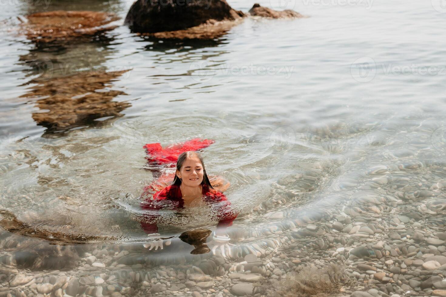 kvinna resa hav. Lycklig turist i röd klänning njut av tar bild utomhus för minnen. kvinna resande Framställ i hav strand, omgiven förbi vulkanisk berg, delning resa äventyr resa foto