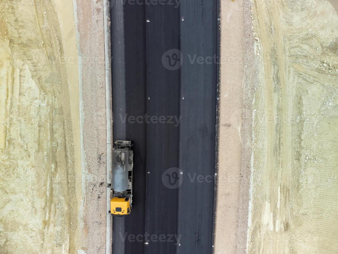 gul lastbil häller bitumen över en ny väg. antenn Drönare skott. väg konstruktion i framsteg på backe natur kanjon. infrastruktur utveckling och logistik. foto