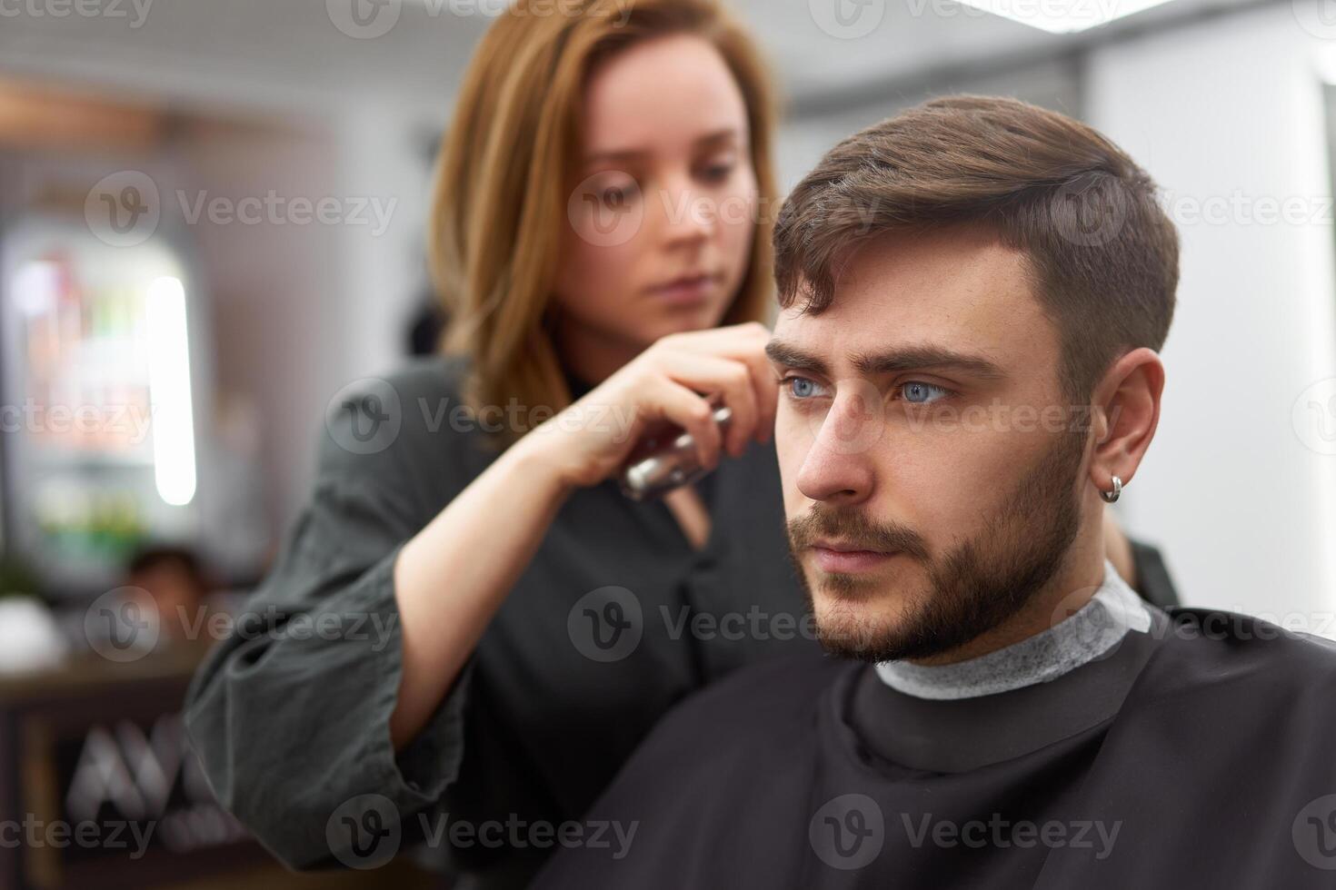 stilig blå ögon man Sammanträde i barberare affär. hårstylist frisör kvinna skärande hans hår. kvinna barberare. foto