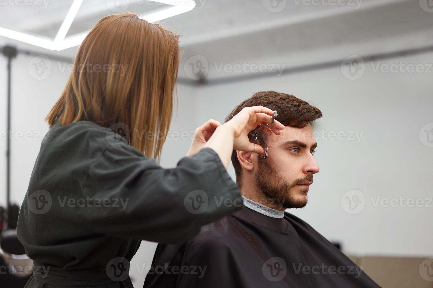 stilig blå ögon man Sammanträde i barberare affär. hårstylist frisör kvinna skärande hans hår. kvinna barberare. foto