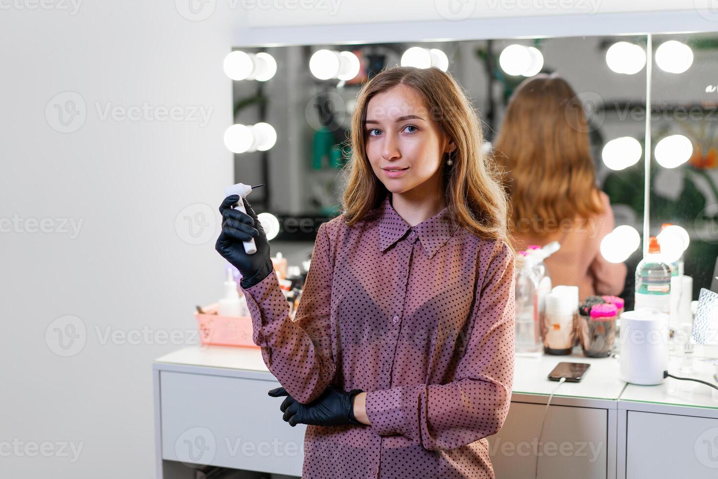 skön ung caucasian smink konstnär stående med verktyg i händer på bakgrund spegel i en skönhet salong. foto
