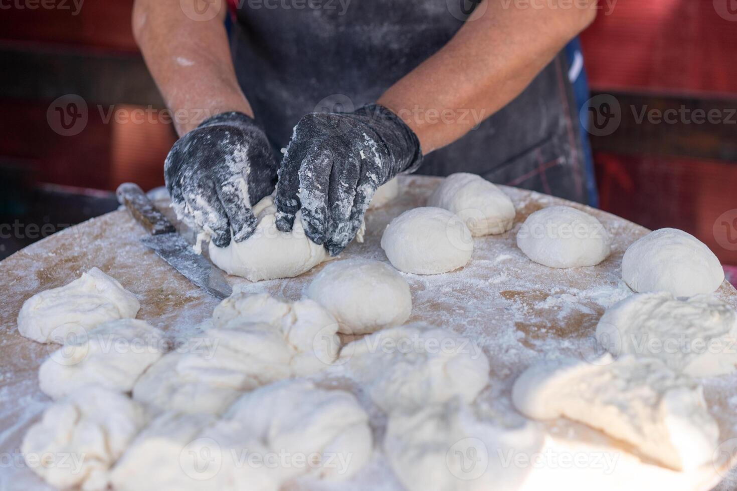 kock i svart handskar nedskärningar rå deg in i bitar göra pizza patties bröd. foto