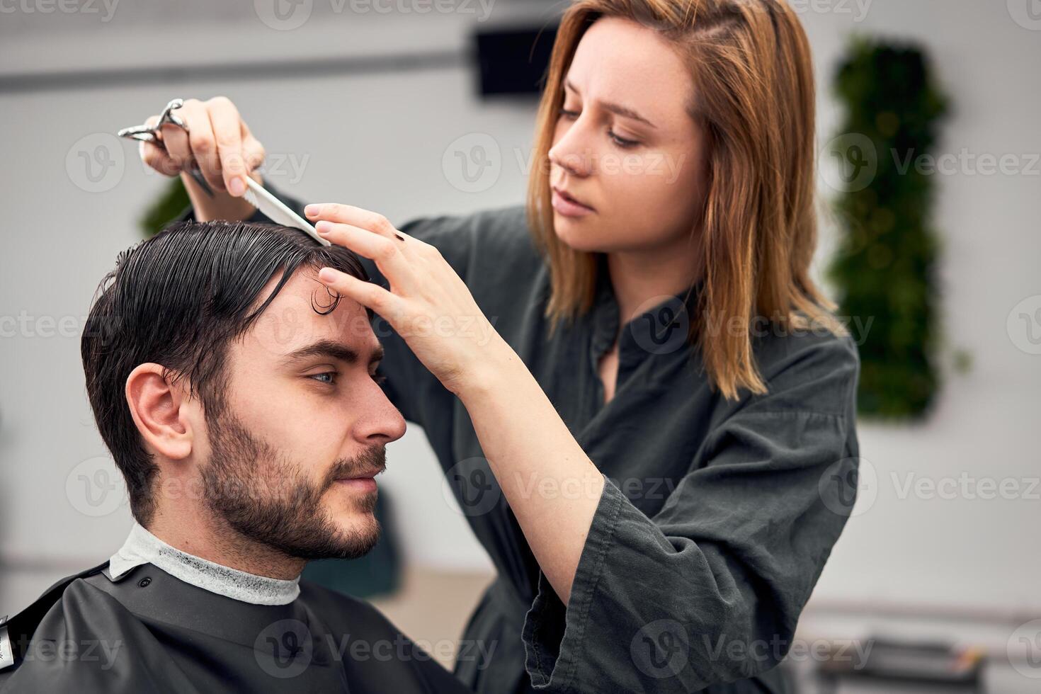 stilig blå ögon man Sammanträde i barberare affär. hårstylist frisör kvinna skärande hans hår. kvinna barberare. foto