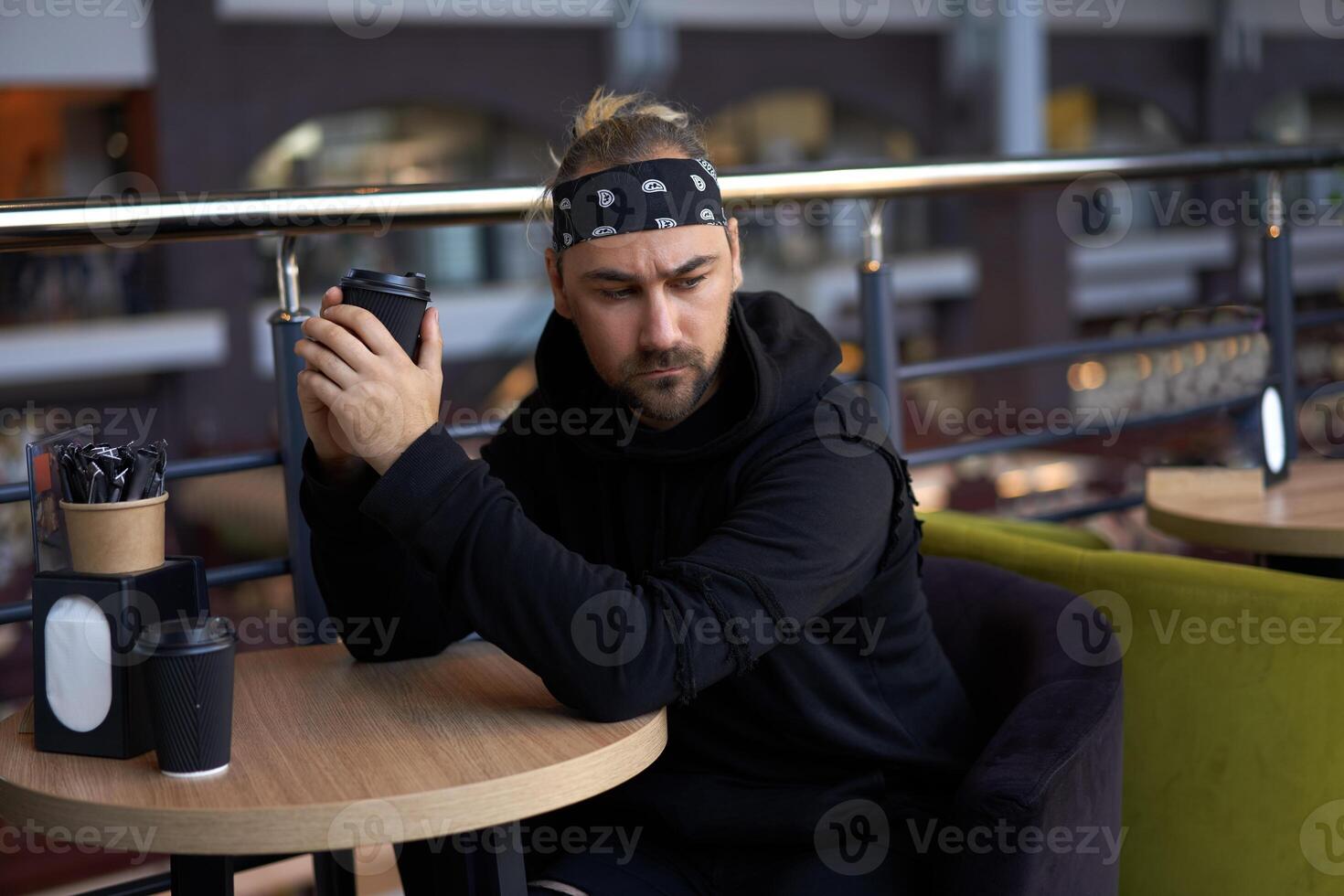 ung stilig ensam man sitter Kafé tabell ledsen väntar för möte dricka kaffe från en papper kopp. foto