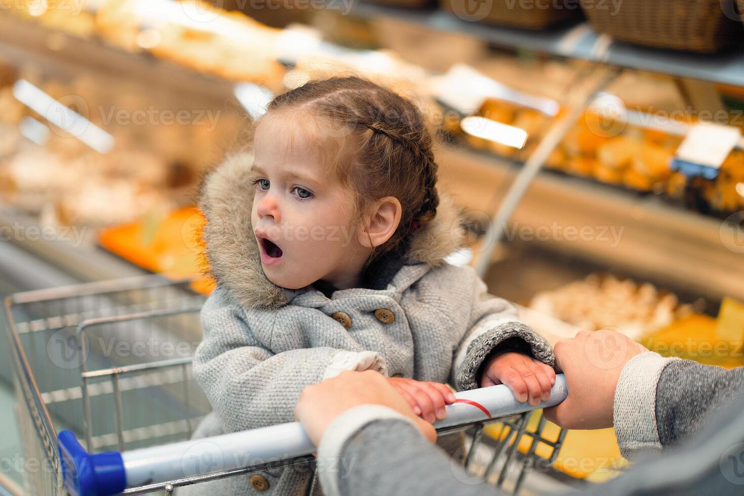 liten flicka öppnad henne mun i överraskning medan Sammanträde i en mataffär vagn foto