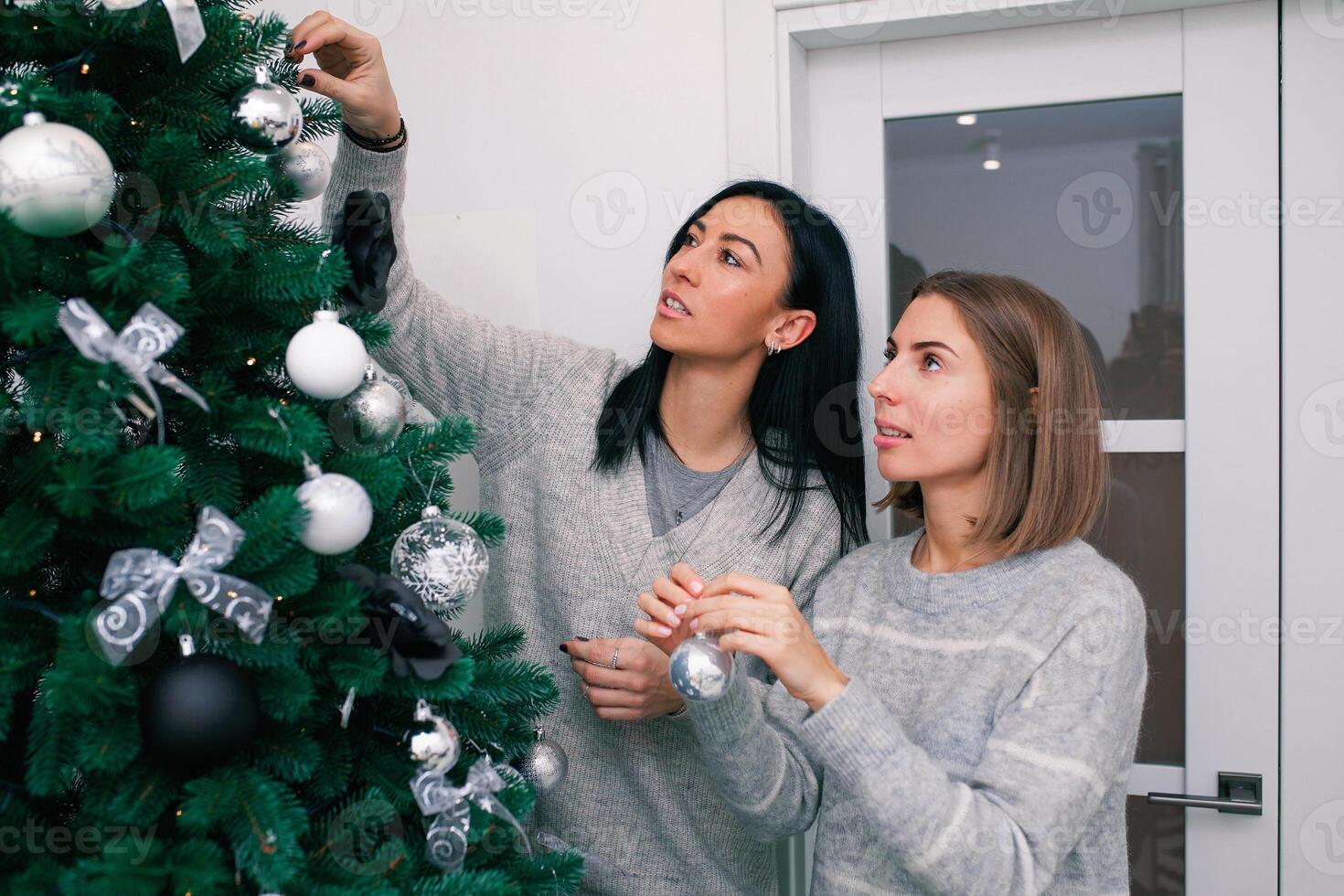 två ung kvinnor dekorera de jul träd, framställning för de ny år firande foto