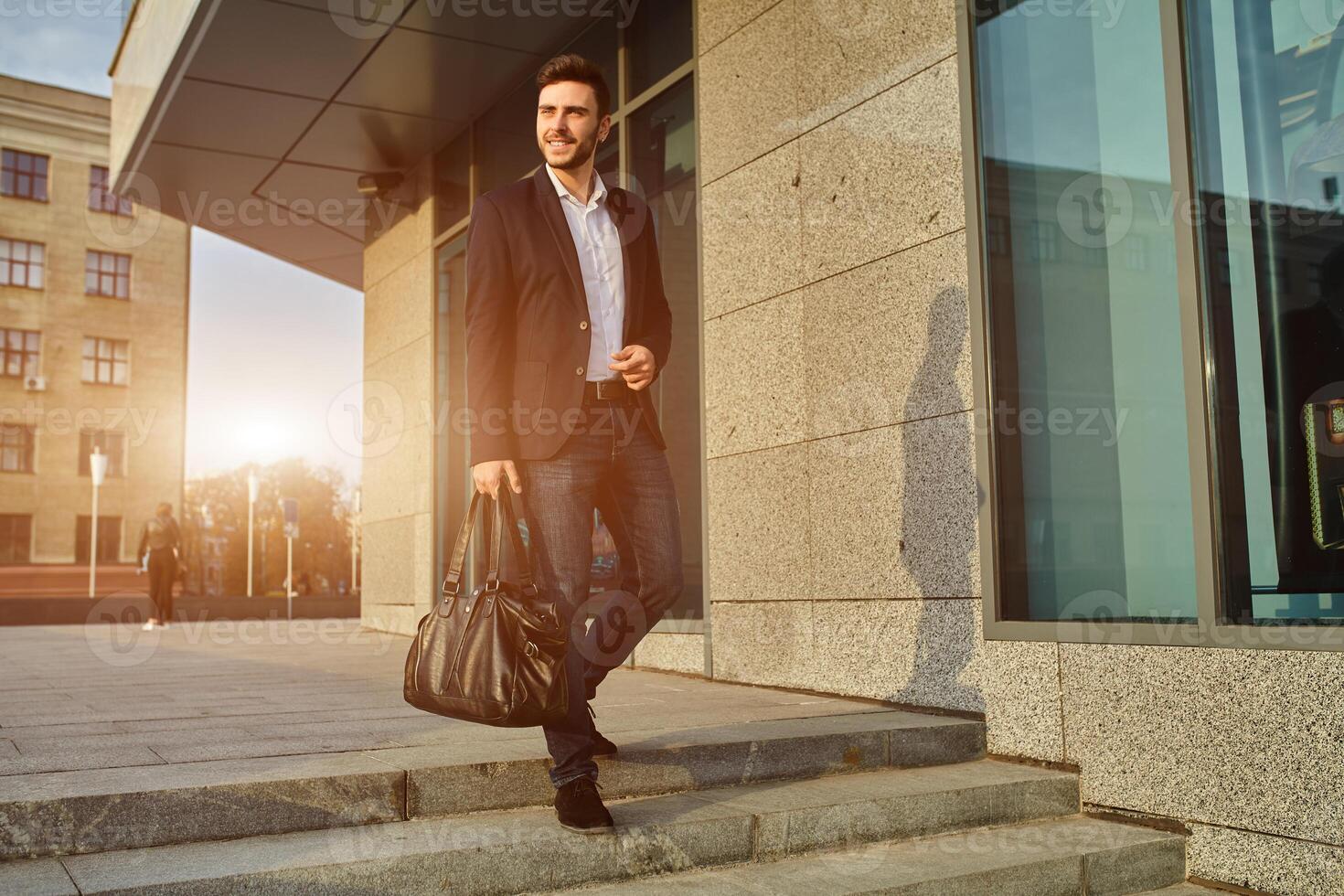 herr- mode. en ung manlig affärsman i en trendig kostym och en vit skjorta med en stor svart handväska kommer ut från en modern Kläder Lagra. foto