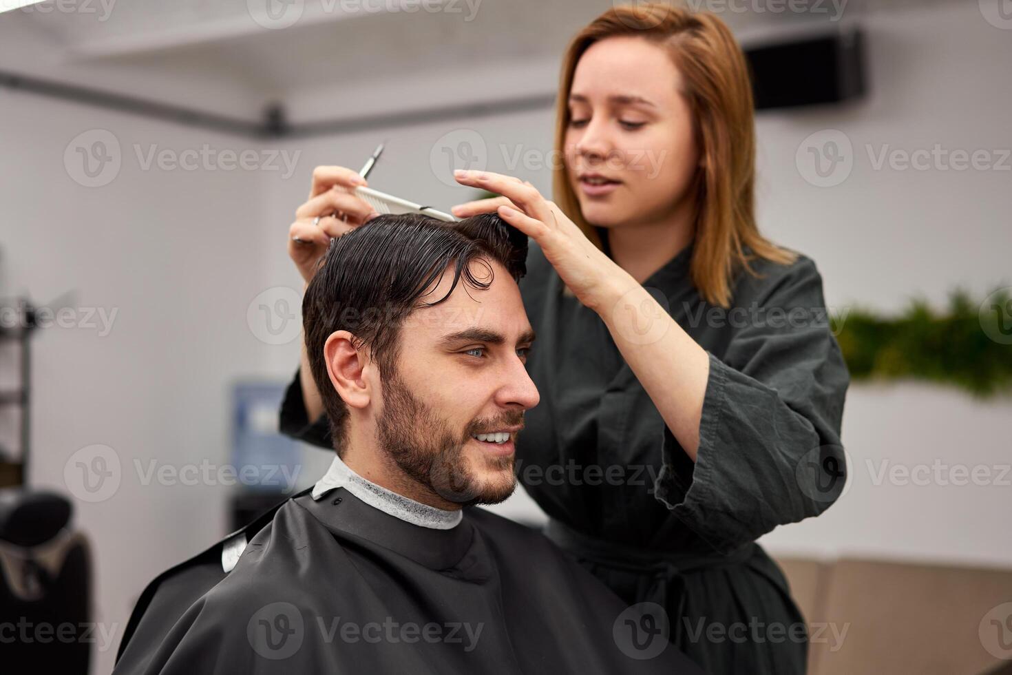 stilig blå ögon man Sammanträde i barberare affär. hårstylist frisör kvinna skärande hans hår. kvinna barberare. foto