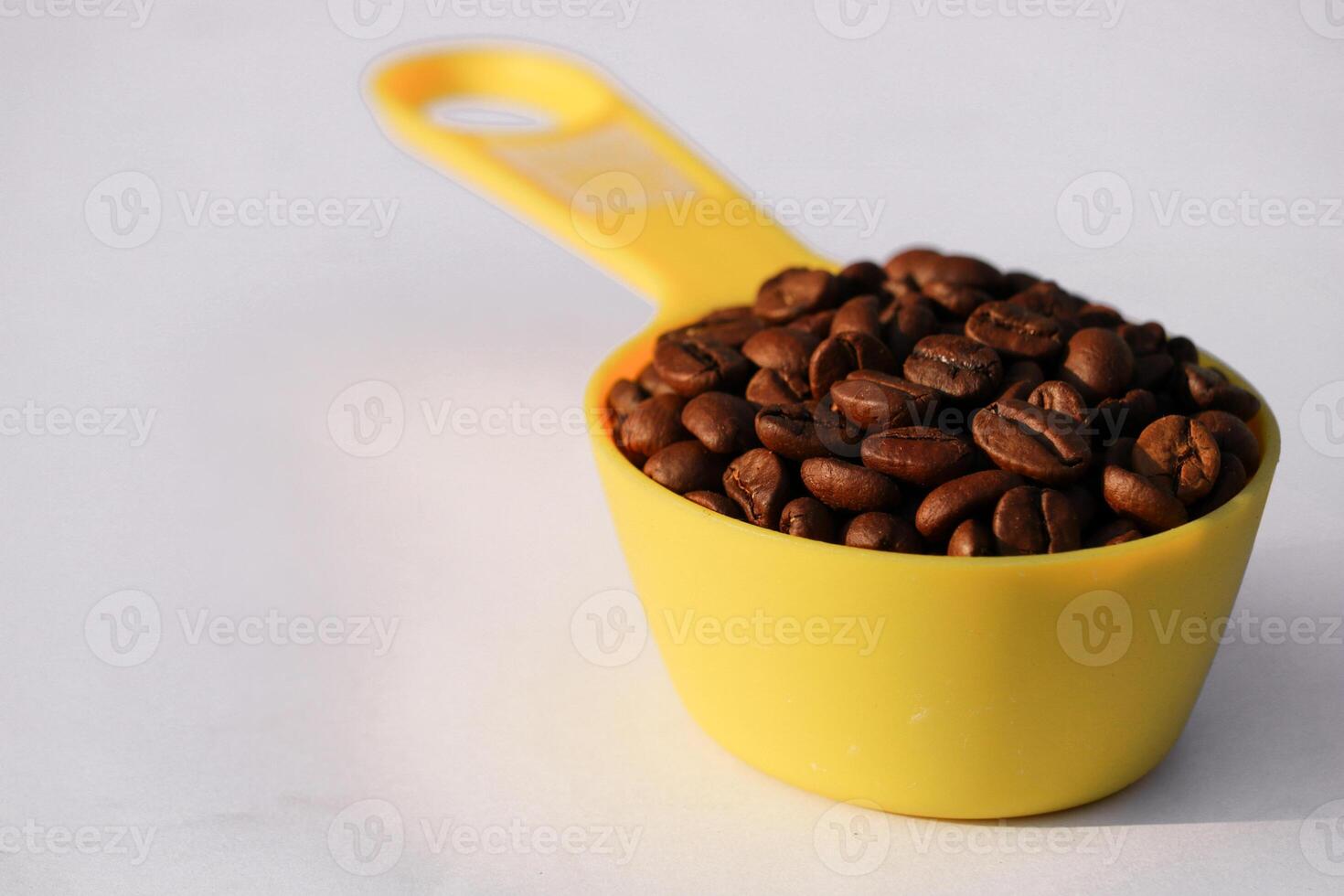 rostad kaffe bönor i gul mätning kopp på isolerat bakgrund. stänga upp av kaffe bönor i mätning kopp. foto