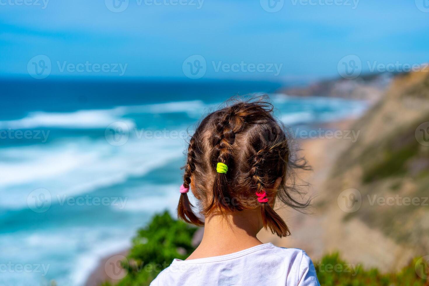 liten flicka ser tropisk sandig strand och hav med turkos vatten med vågor. foto