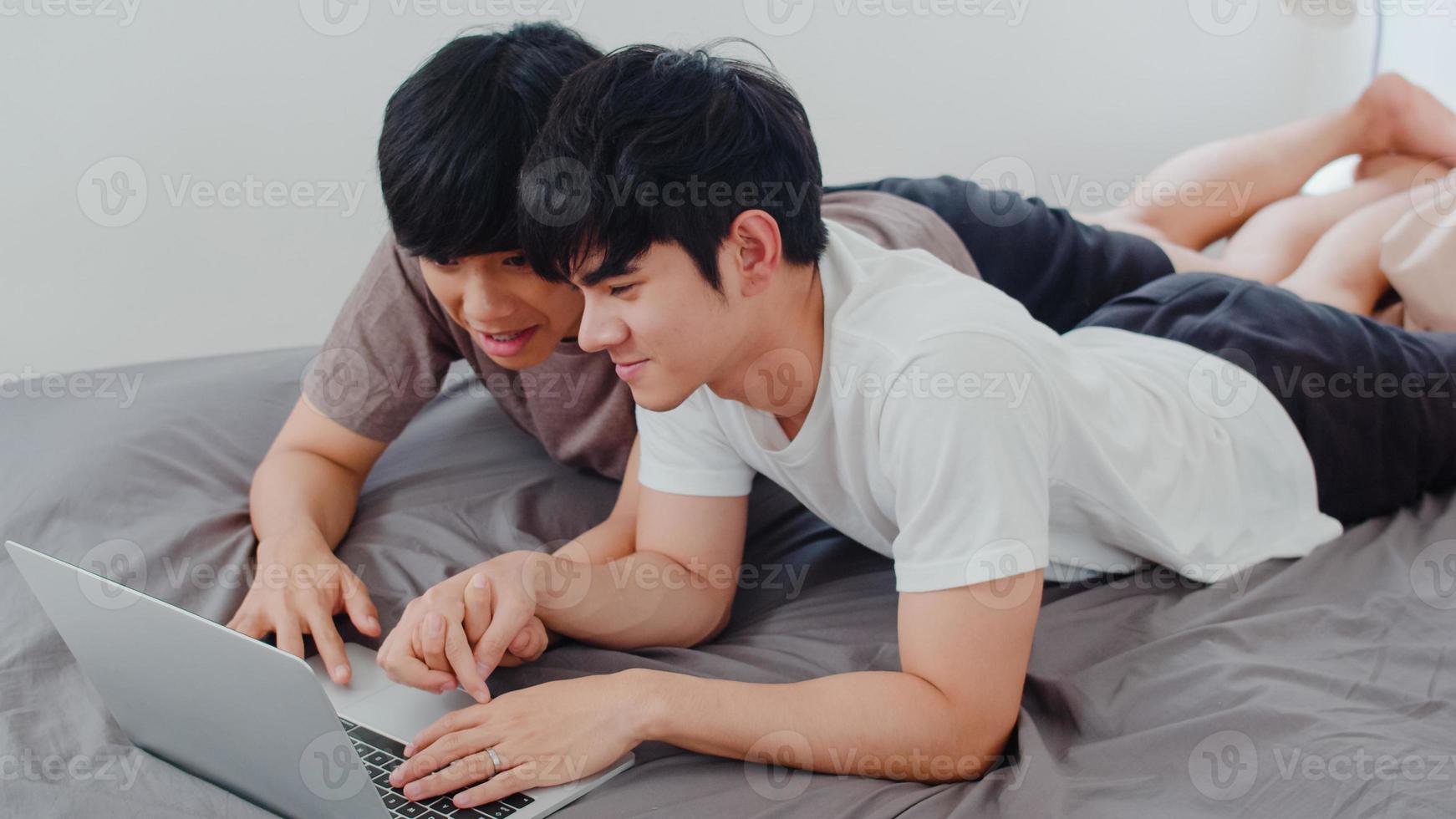 Asiatiska homosexuella hbtq män par använder dator bärbar dator i moderna hem. ung asien älskare manlig glad slappna av vila tillsammans efter att ha vaknat, titta på film liggande på sängen i sovrummet hemma på morgonen koncept. foto