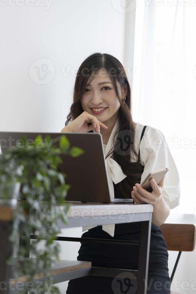en japansk kvinna kontroll smartphone förbi avlägsen arbete i de små kontor foto