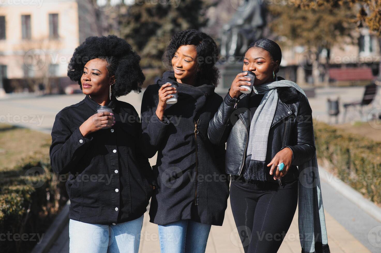 tre skön och eleganta mörkhyad flickor med lång hår stående i en stad och dricka en kaffe och använda sig av de telefoner foto