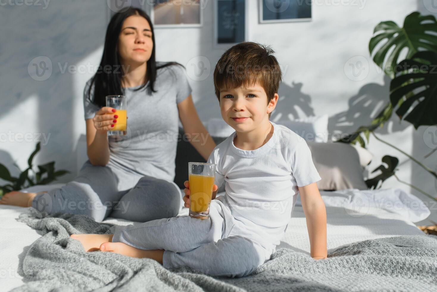 mamma med son i pyjamas dricka juice i de morgon- i säng. friska äter begrepp foto