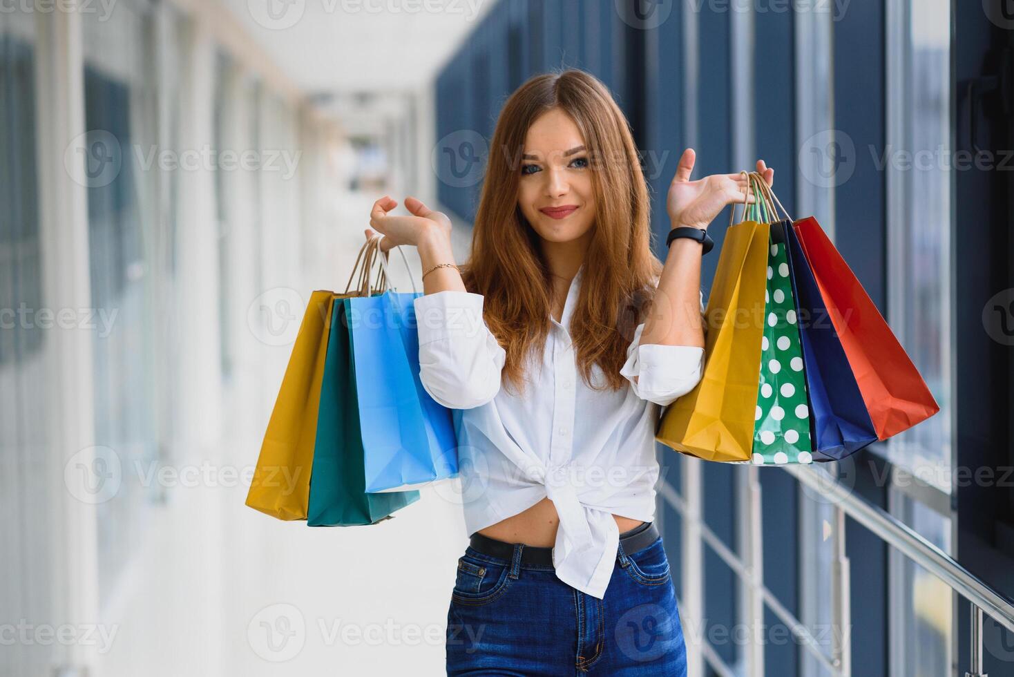 lycka, konsumentism, försäljning och folkbegrepp - le ung kvinna med shoppingkassar över gallerian bakgrund foto