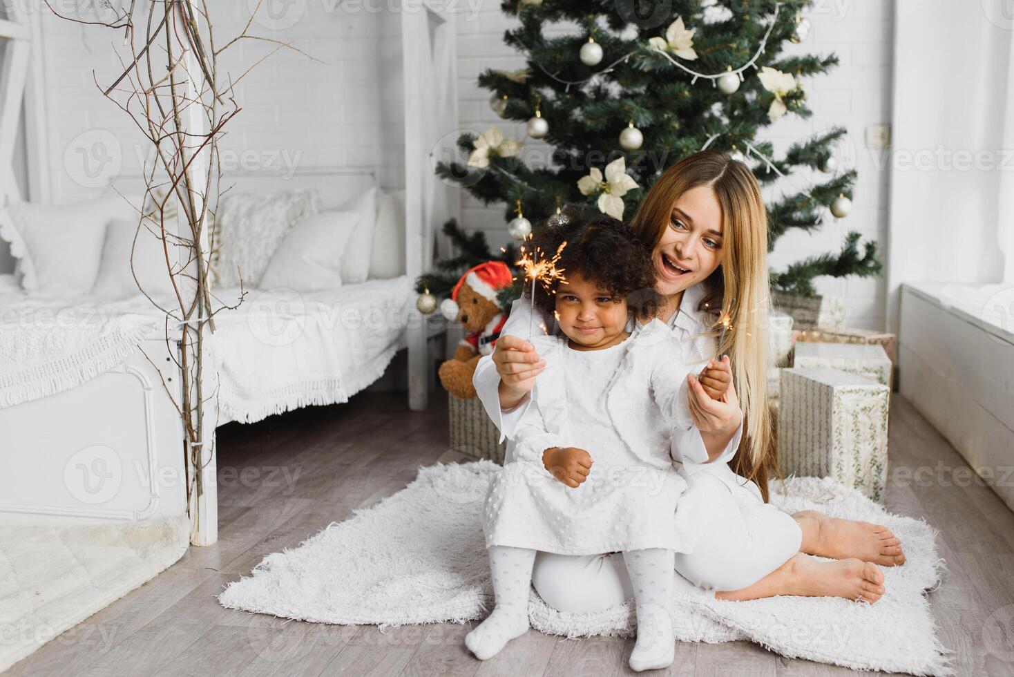 glad jul och Lycklig högtider glad mamma och henne söt dotter på jul träd. förälder och liten barn har roligt nära jul träd inomhus. kärleksfull familj med presenterar i rum. foto