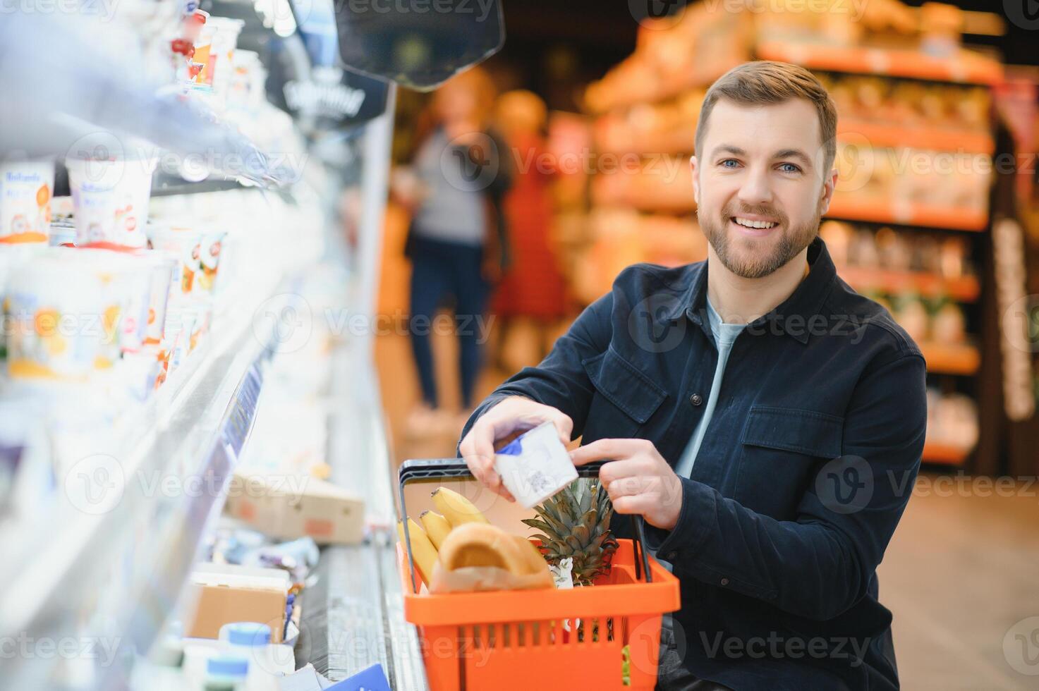 kund i mataffär. man håller på med matvaror handla stående med vagn välja mat produkt inomhus. kille uppköp specerier i mat Lagra. selektiv fokus, kopia Plats. foto