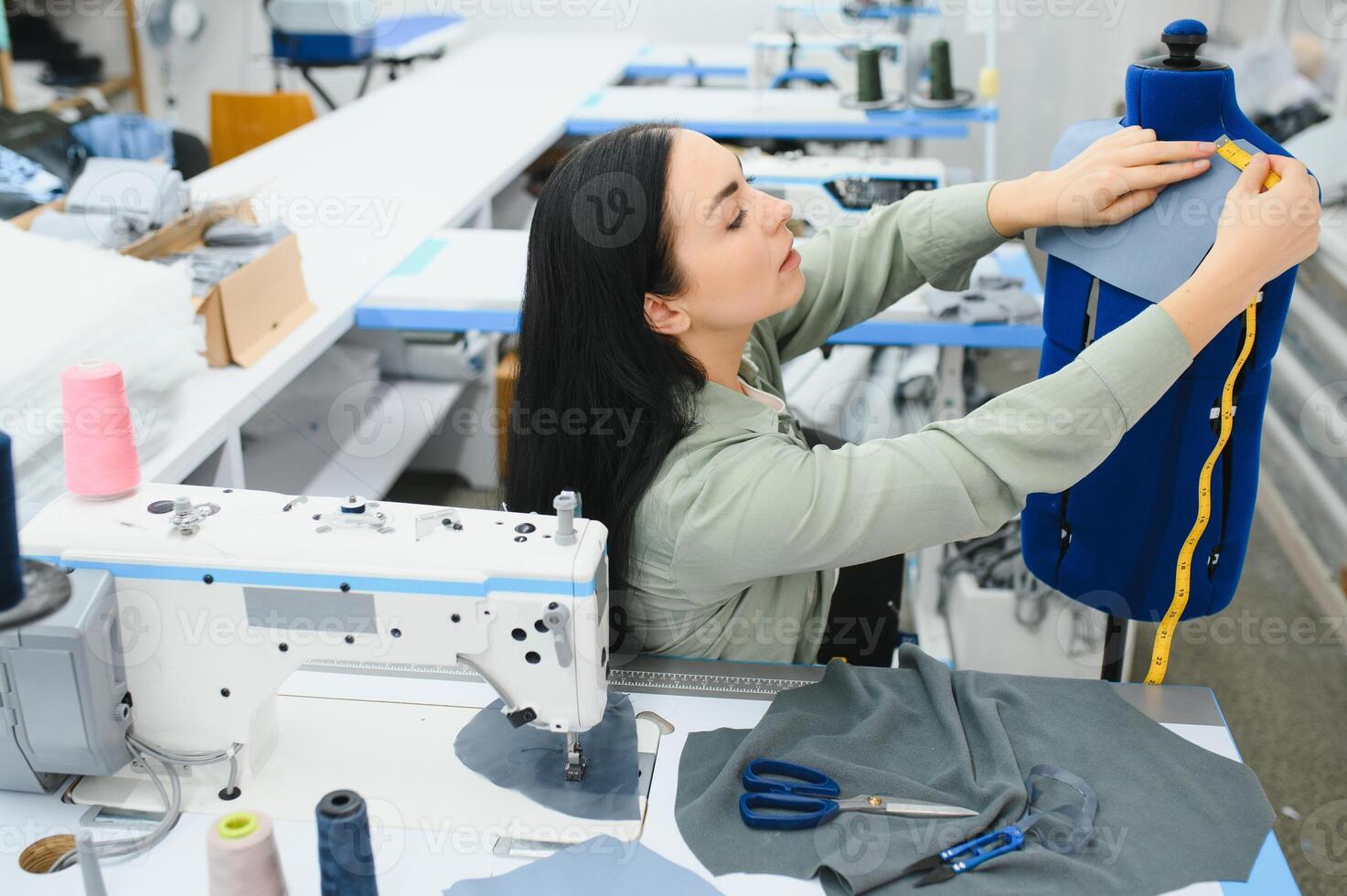 porträtt av en skön sömmerska bärande en tejp mäta och arbetssätt i en textil- fabrik foto