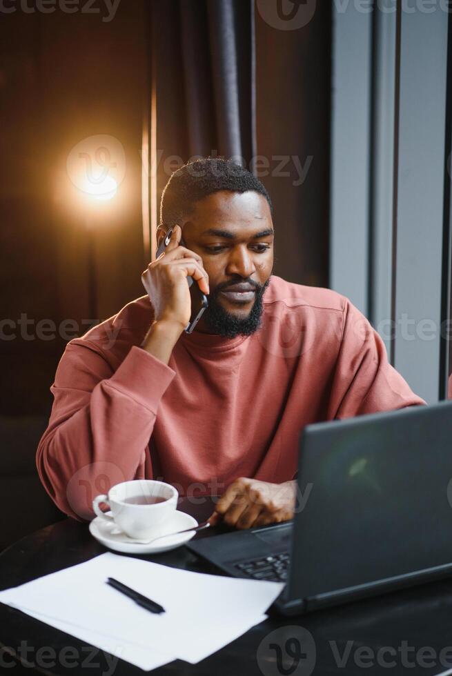 affärsman använder sig av telefon arbetssätt på bärbar dator i kaffe affär. foto