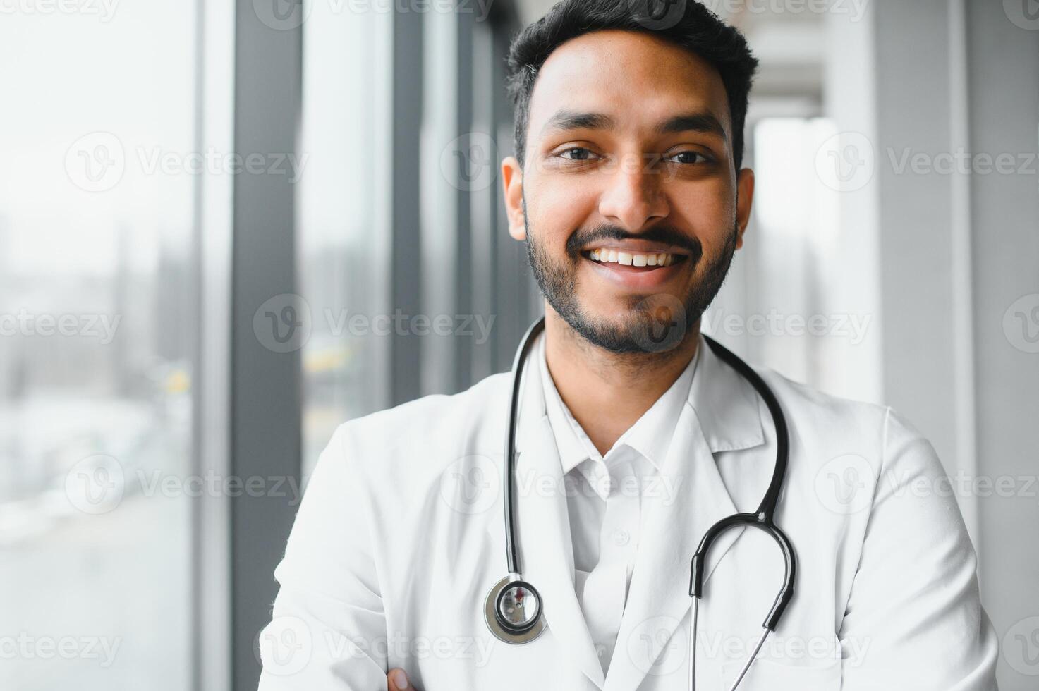 porträtt av Lycklig vänlig manlig indisk latin läkare medicinsk arbetstagare bär vit täcka med stetoskop runt om nacke stående i modern privat klinik ser på kamera. medicinsk sjukvård begrepp foto