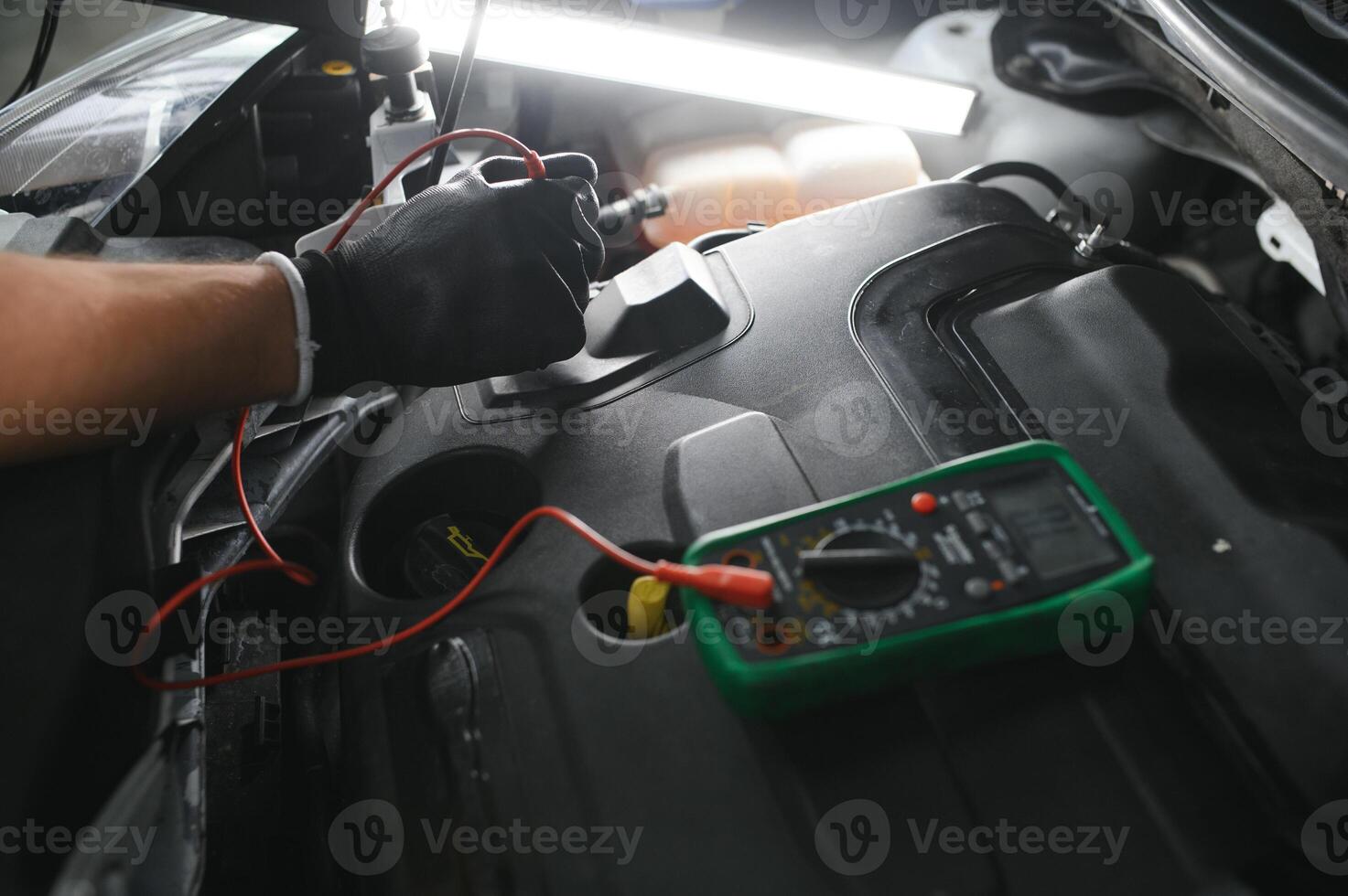 bil mekaniker är använder sig av en multimeter med Spänning räckvidd mått till kolla upp de Spänning nivå av de bil batteri. foto