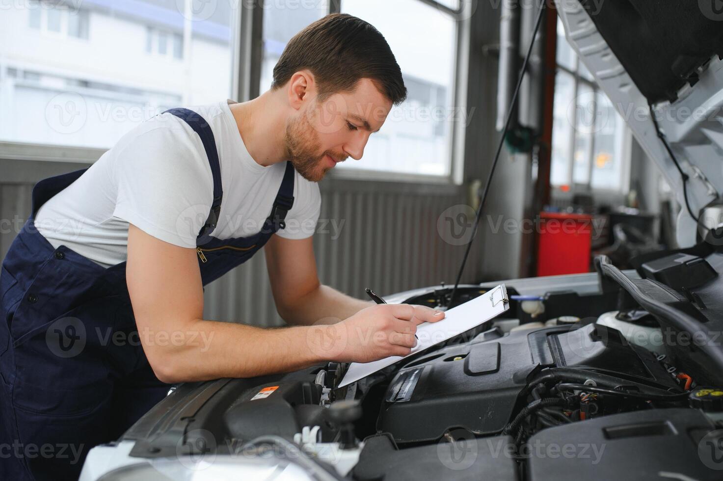 koncentrerad mekaniker skrivning på Urklipp på de reparera garage foto