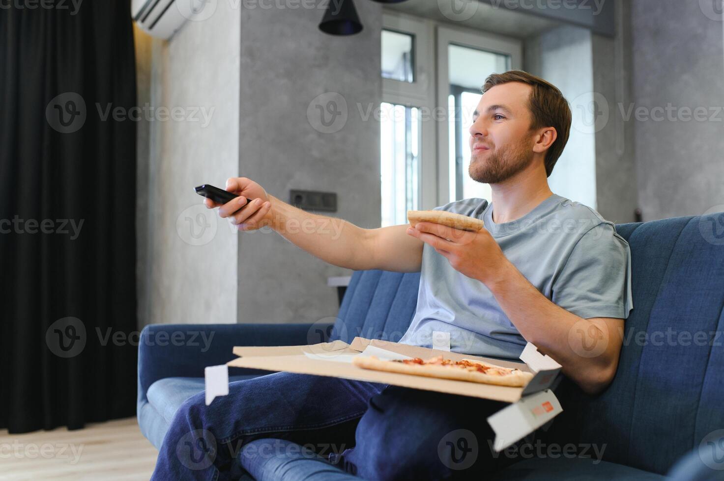 resten efter hård arbete. en man är Sammanträde på de soffa på Hem, äter pizza och tittar på tv. foto