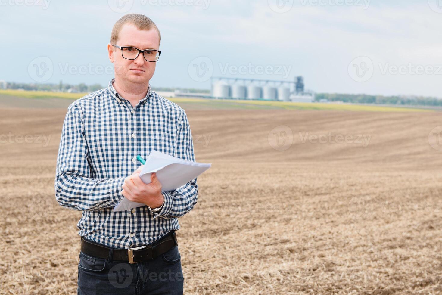 modern jordbrukare kontroll hans fält växt mot majs torktumlare silos i begrepp av industriell och lantbruk foto